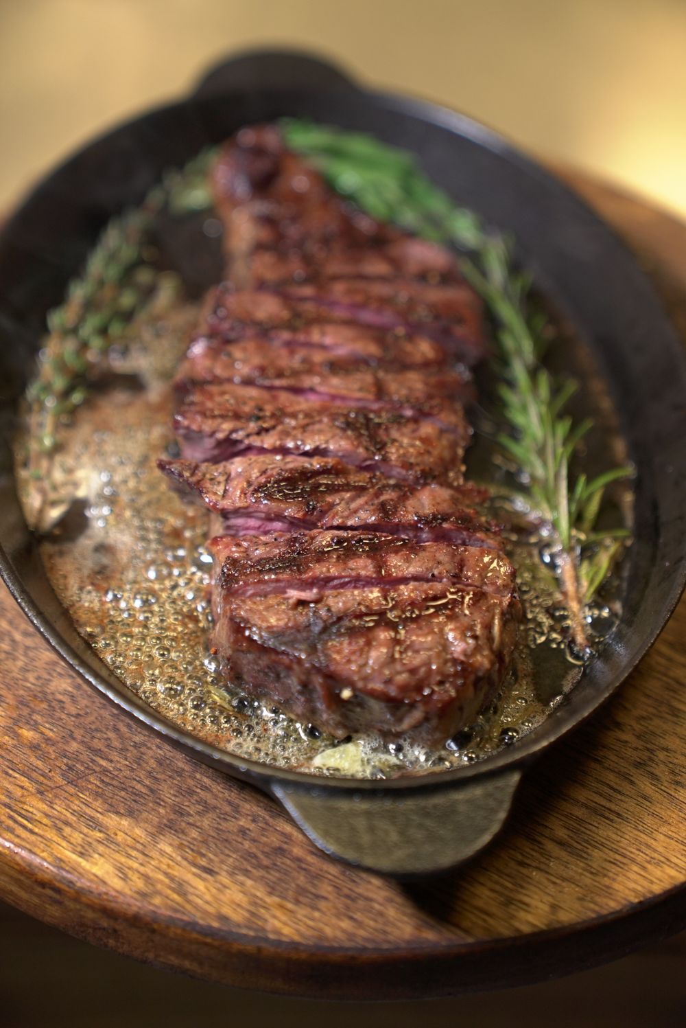 Bison steak searing in a hot cast iron pan with rosemary