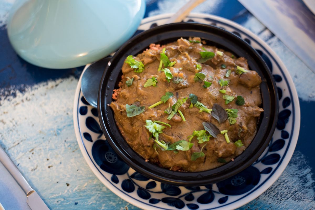 Bowl of braised goat shoulder in preserved lemon and olive sauce with cilantro
