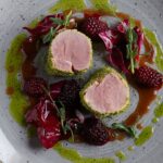 Sliced grilled pork tenderloin fanned on a plate with a glossy pan sauce