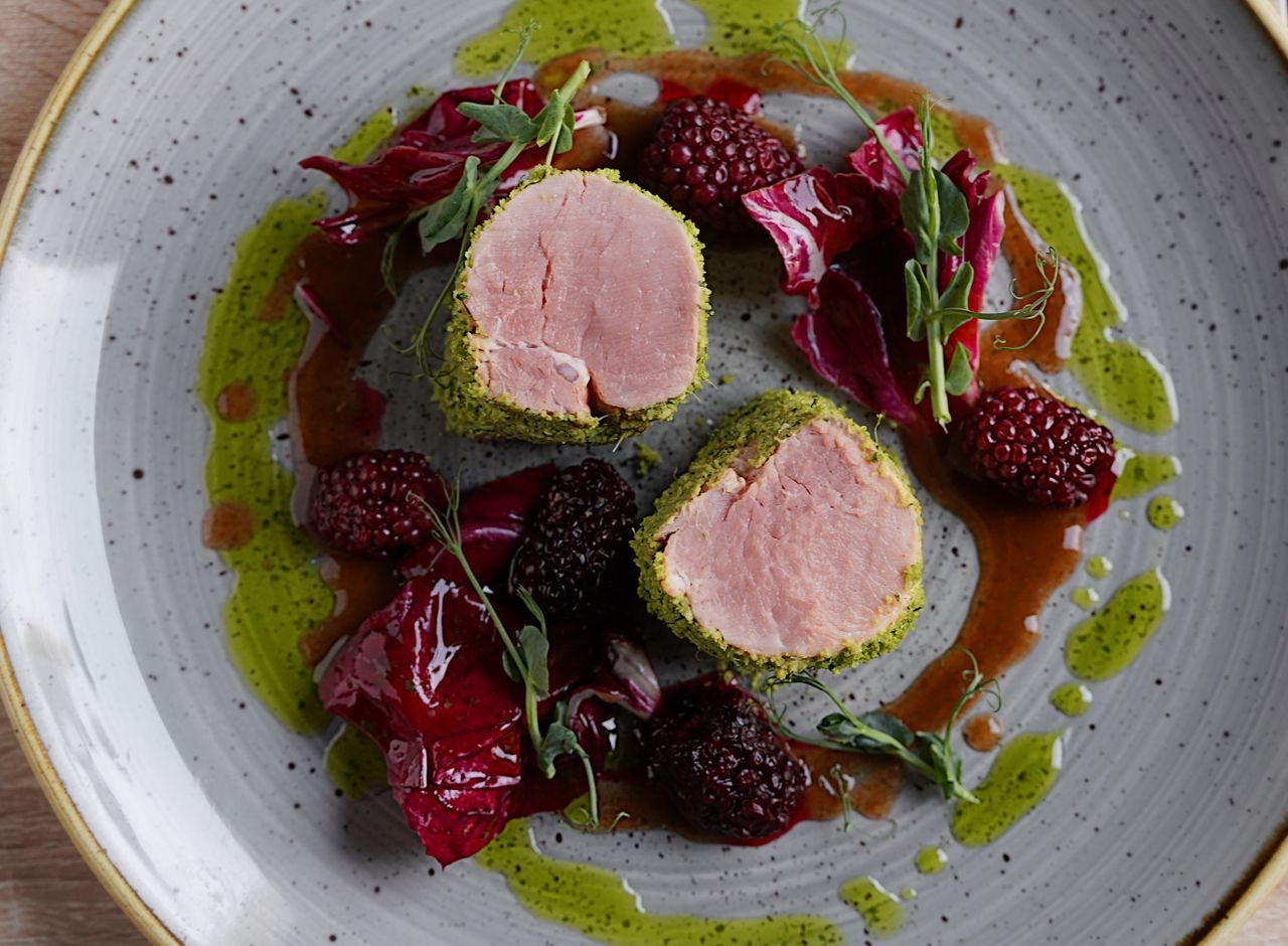 Sliced grilled pork tenderloin fanned on a plate with a glossy pan sauce