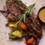 Garlic and herb roast leg of lamb resting on a platter with roasted vegetables