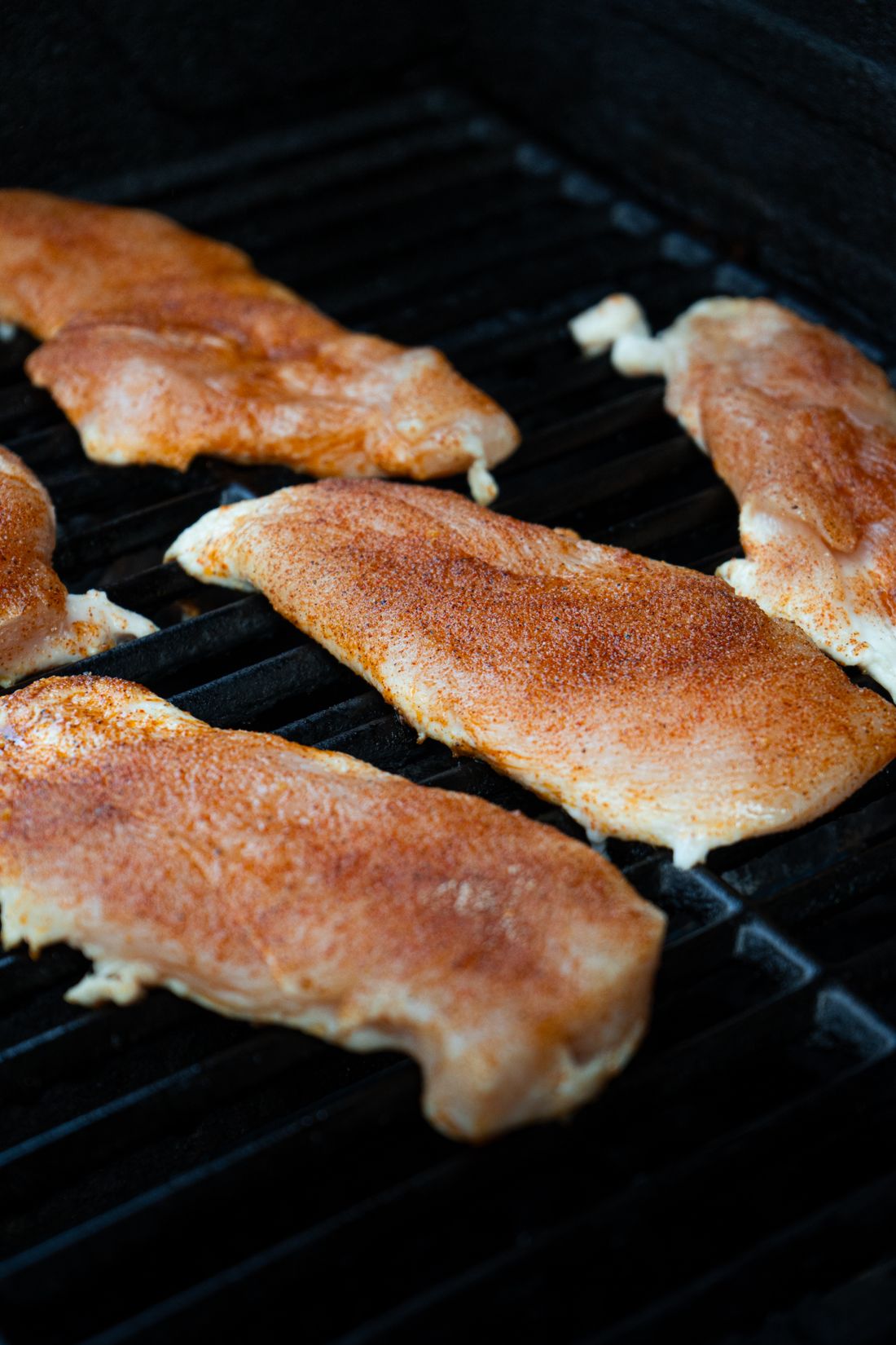 Seasoned boneless chicken breasts searing on a hot outdoor grill