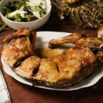 Slow-roasted goat leg carved on a rustic wooden board with fresh salad