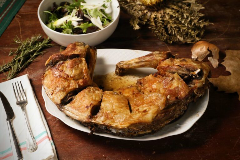 Slow-roasted goat leg carved on a rustic wooden board with fresh salad