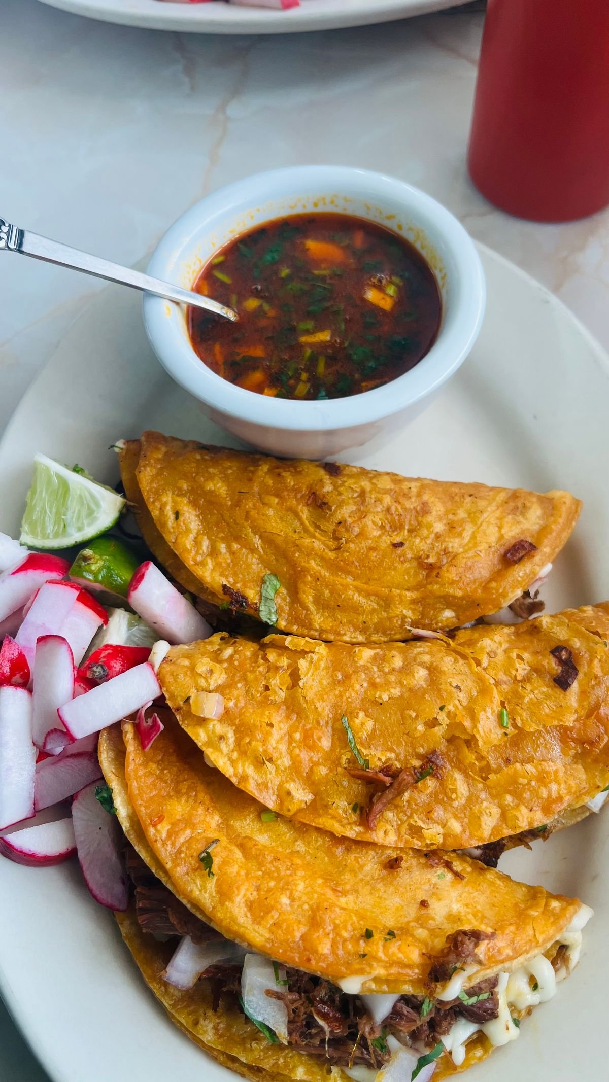 Goat birria tacos with a cup of red consomme for dipping