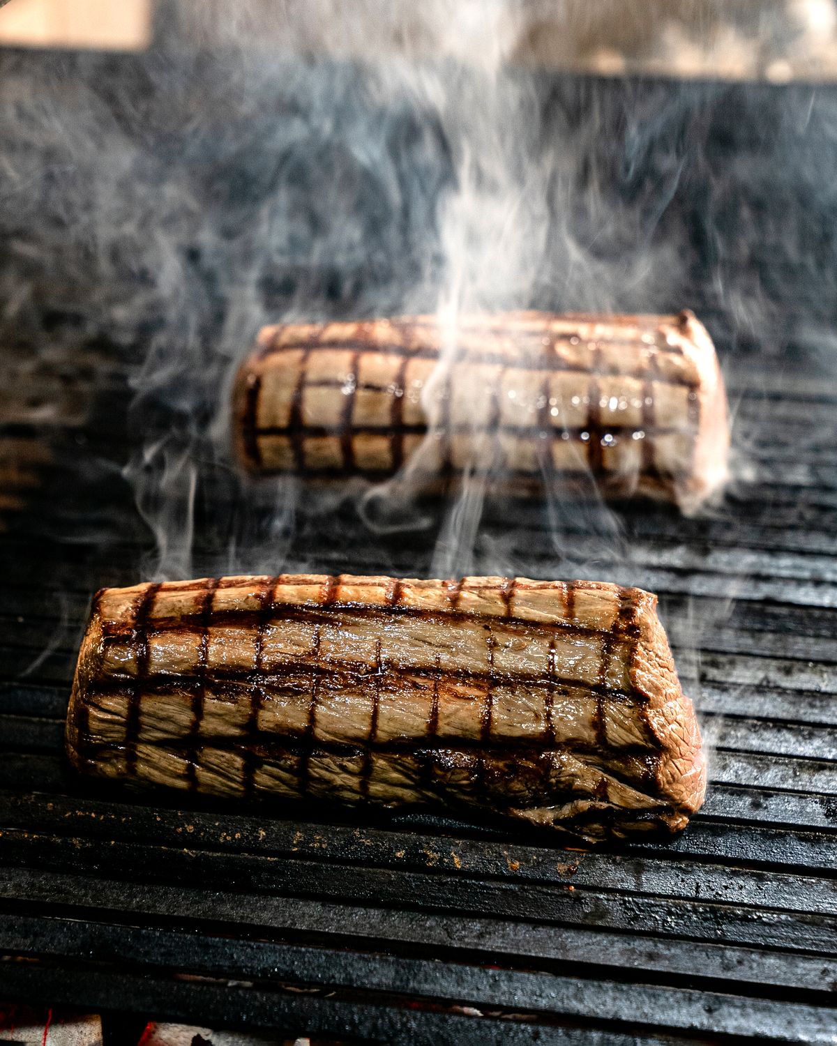 Hanger steak grilling with smoke rising before saucing