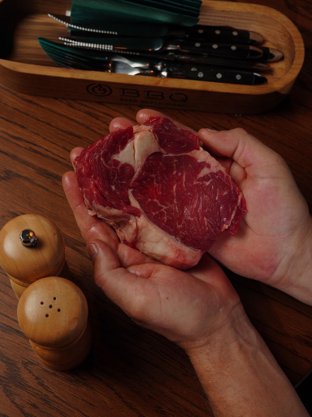 Raw hanger steak held over a wooden board before seasoning