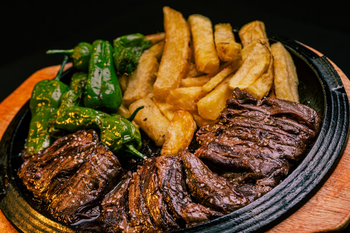 Sliced skillet seared hanger steak plated with fries and peppers