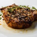 Cast iron pork chop with crispy sage leaves and cider apples on a white plate