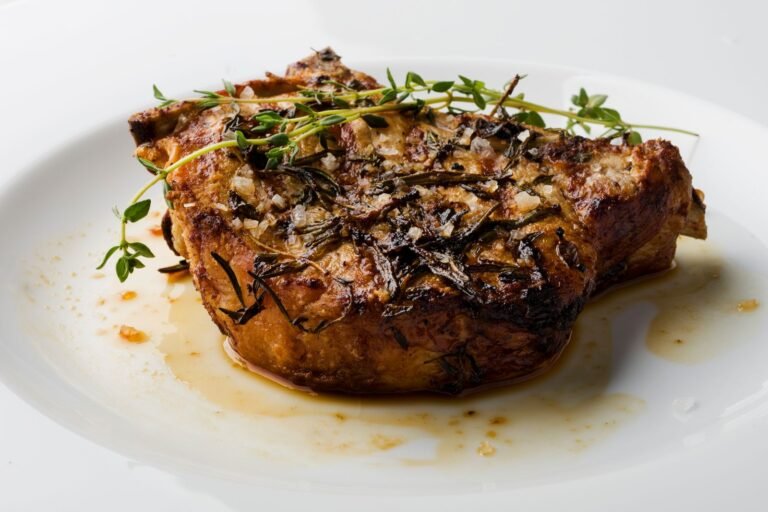 Cast iron pork chop with crispy sage leaves and cider apples on a white plate