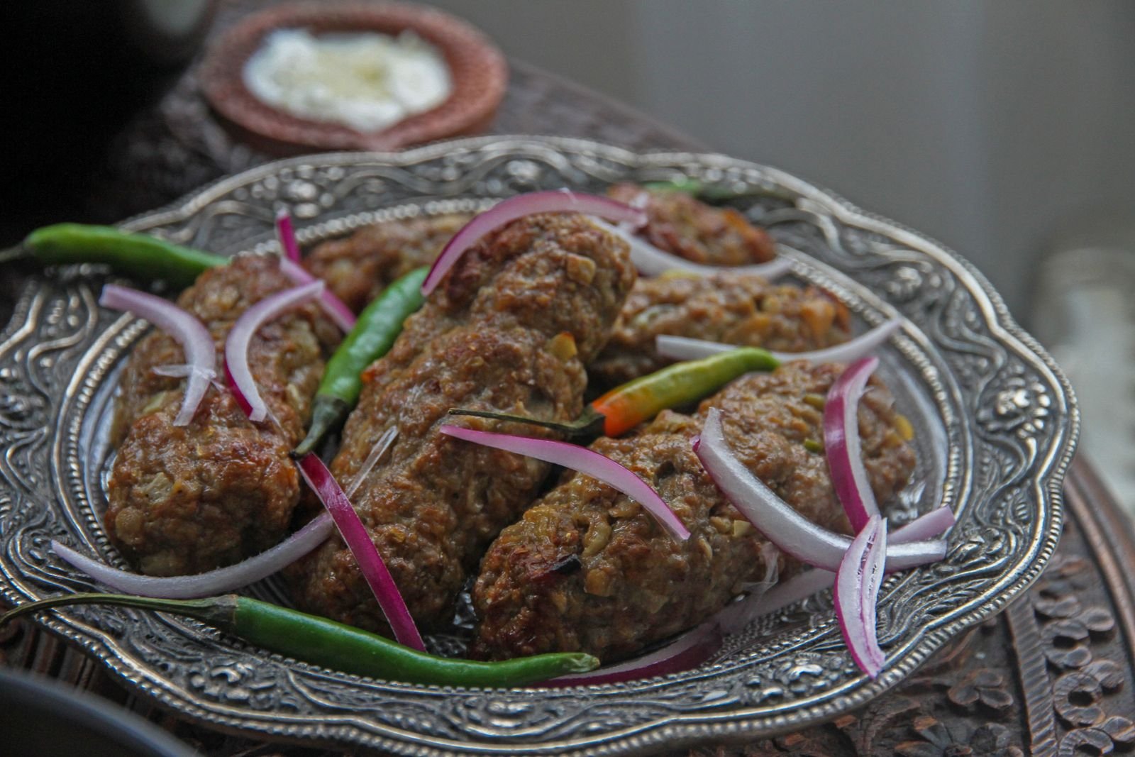Lamb kofta on metal skewers grilling over coals with onions and peppers