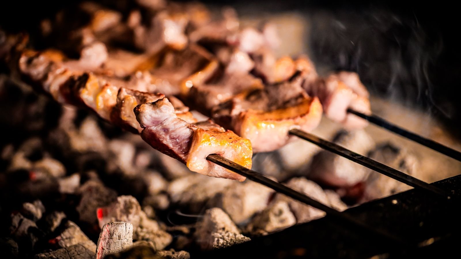 Grilled lamb skewers charring over hot coals ready for zhoug and pickled onion