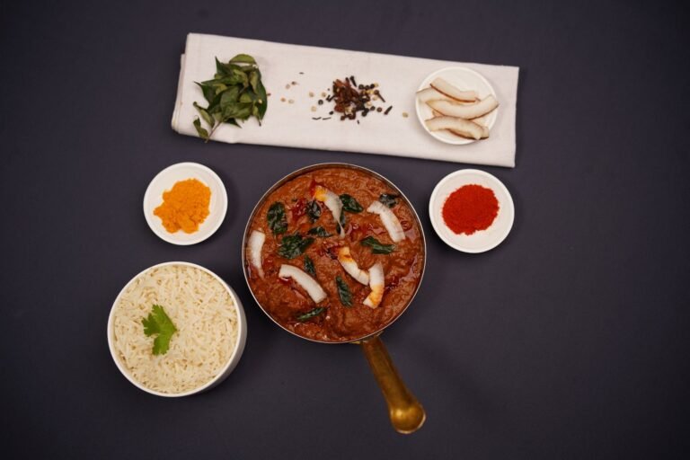 Deep red lamb vindaloo in a serving pot with rice and whole spices