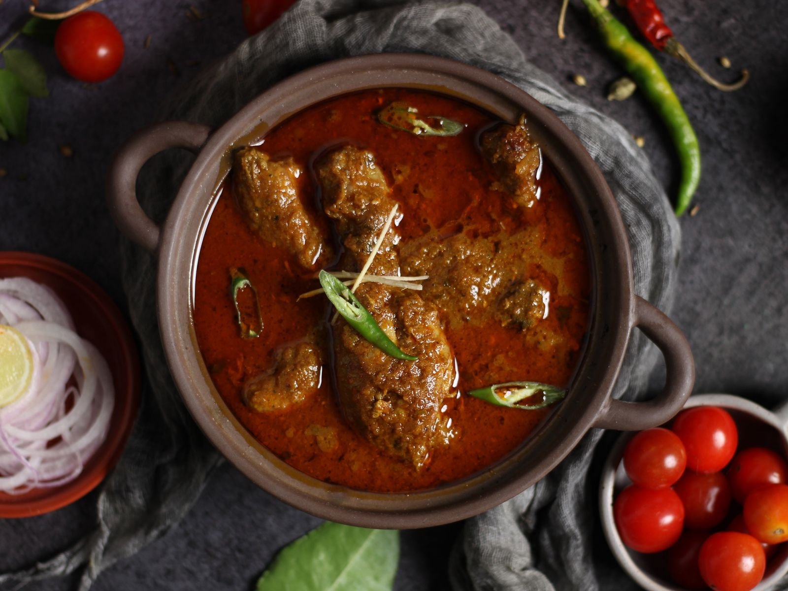 Lamb vindaloo simmered in a clay pot with a layer of red oil on top