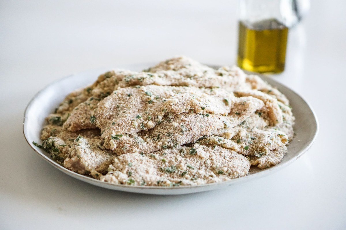 Breaded veal cutlets resting on a plate before frying for veal Milanese