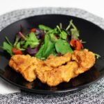 Veal Milanese cutlet on a dark plate with a marinated mushroom and arugula salad