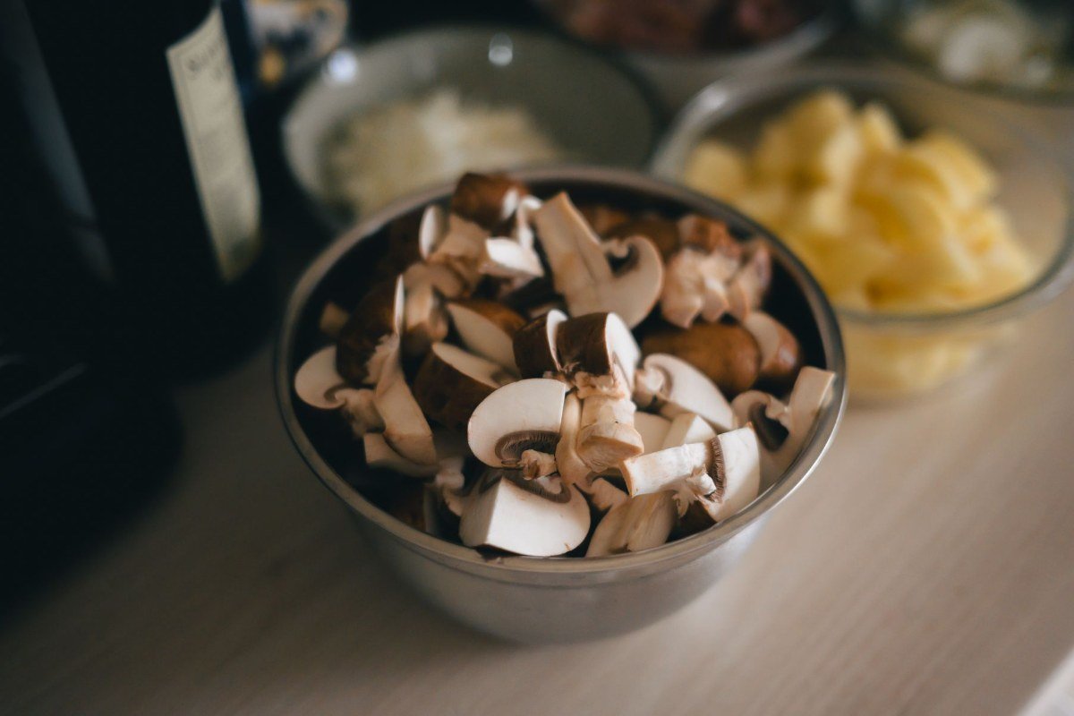 Sliced cremini mushrooms in a metal bowl before marinating for the veal Milanese salad