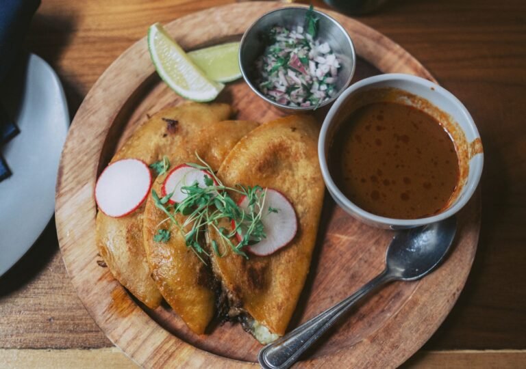 Crisp folded beef tacos on a plate with a cup of red consommé, radish and lime