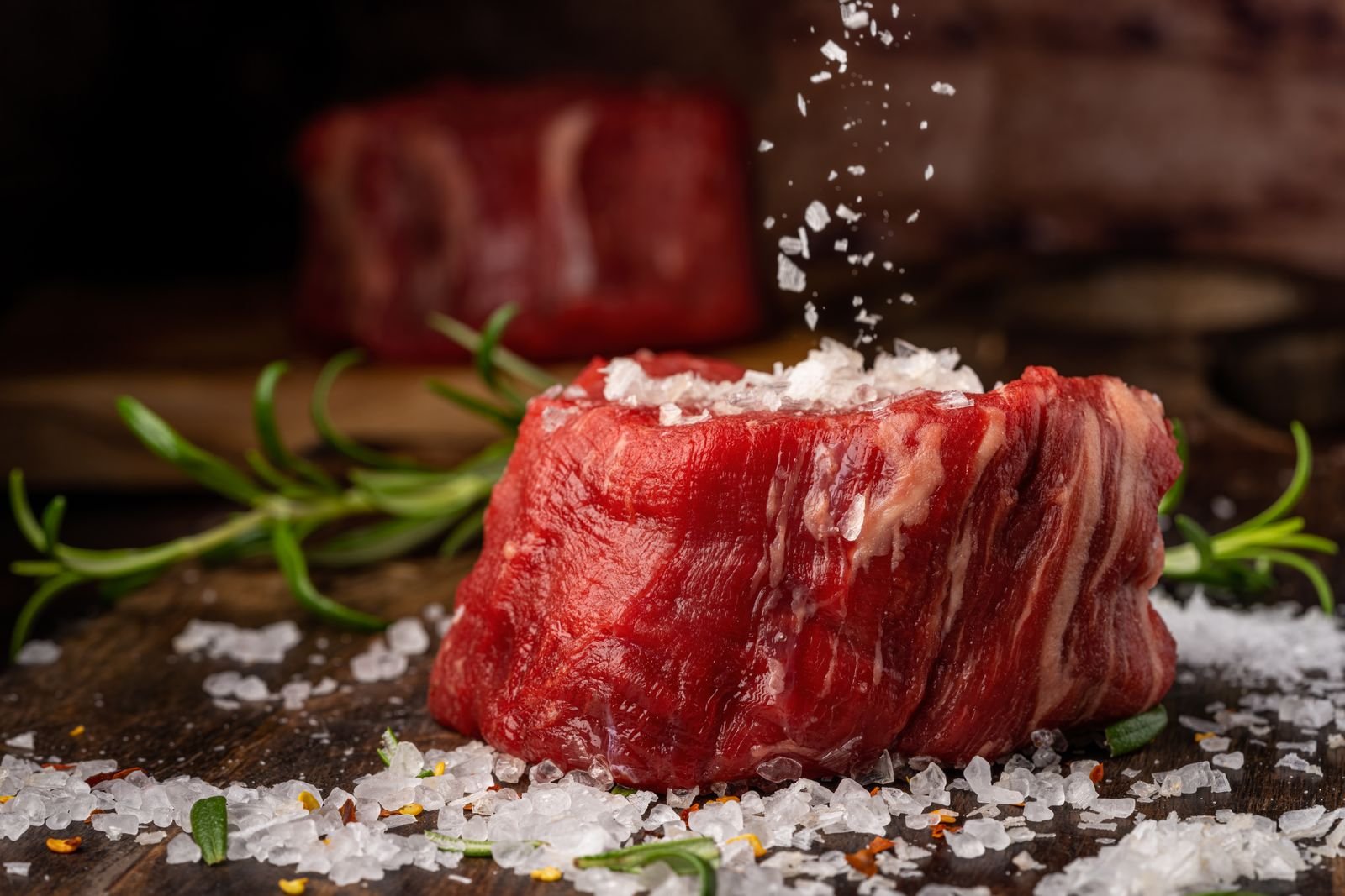 Raw center cut beef tenderloin steak seasoned with sea salt and herbs on a wooden board