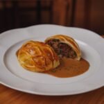 Sliced beef wellington showing the pink tenderloin and pastry crust, served with sauce on a white plate
