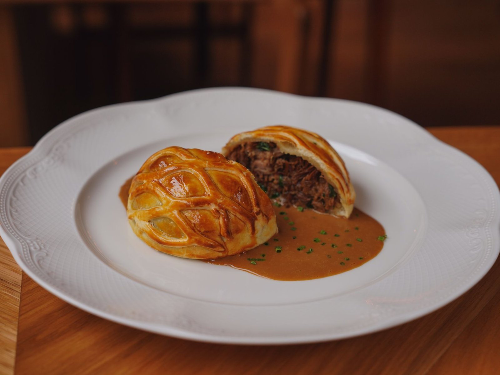Sliced beef wellington showing the pink tenderloin and pastry crust, served with sauce on a white plate