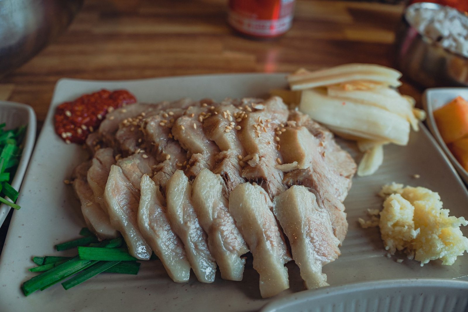 Sliced Korean bossam pork arranged on a platter with kimchi and garlic