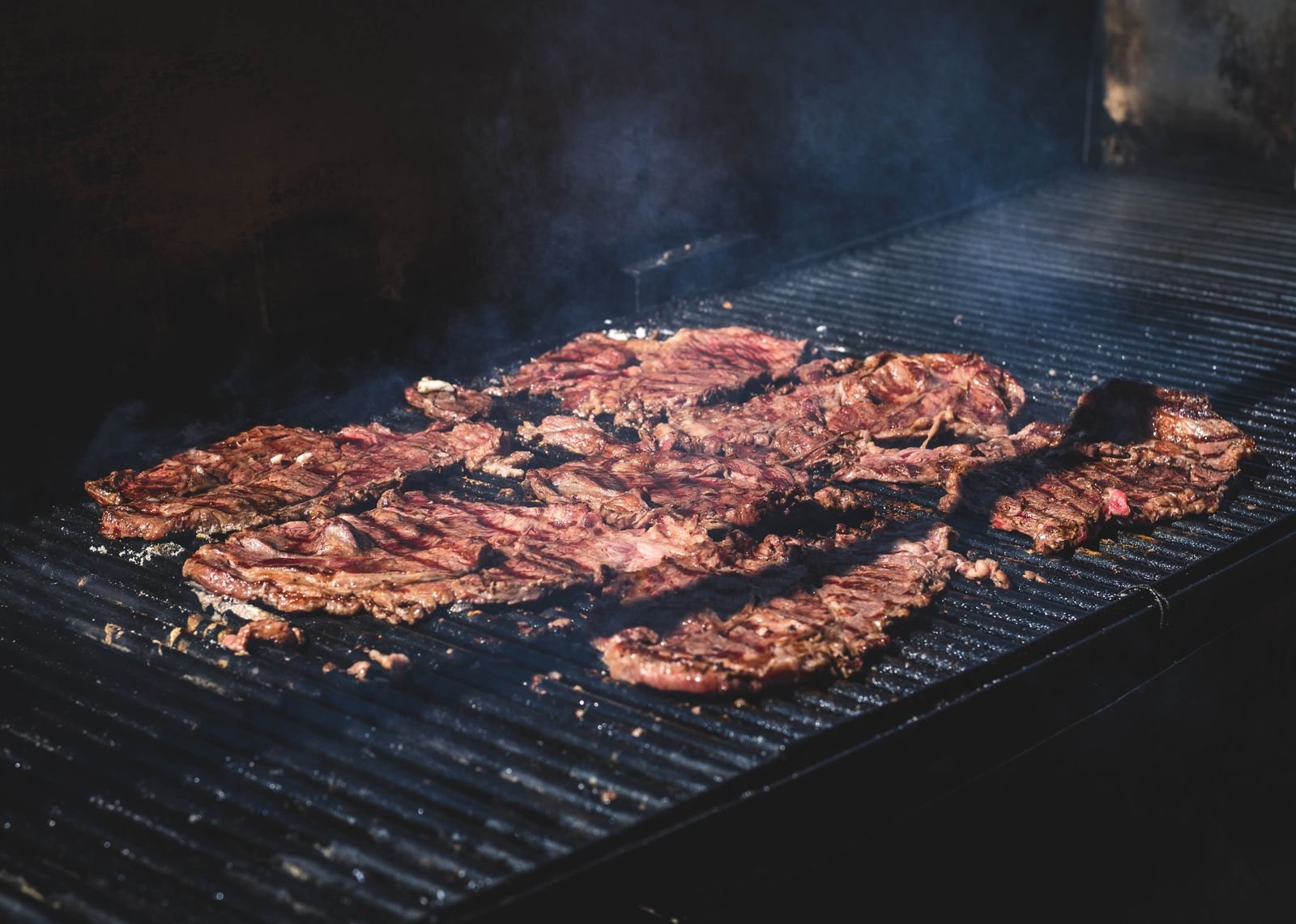 Skirt steak for carne asada searing over a hot grill with smoke rising