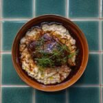 Coq au vin with dark red wine sauce served over mashed potatoes in a bowl on a tiled surface