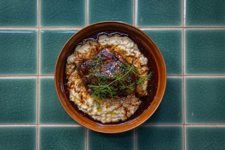 Coq au vin with dark red wine sauce served over mashed potatoes in a bowl on a tiled surface