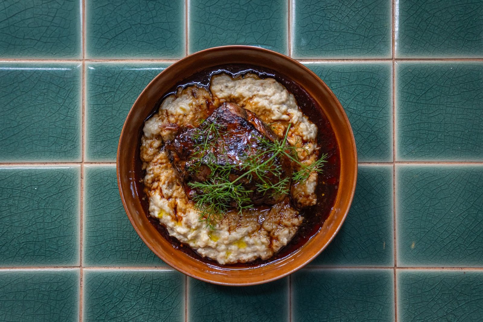 Coq au vin with dark red wine sauce served over mashed potatoes in a bowl on a tiled surface