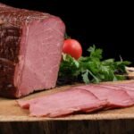 Thin slices of pink cured beef fanned on a wooden board with fresh herbs and tomatoes