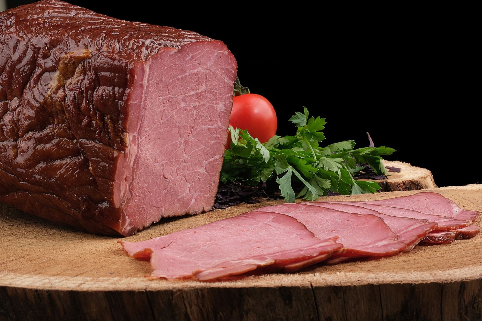 Thin slices of pink cured beef fanned on a wooden board with fresh herbs and tomatoes