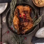 Whole roasted turkey with deep brown skin garnished with cranberries on a wooden table, seen from above