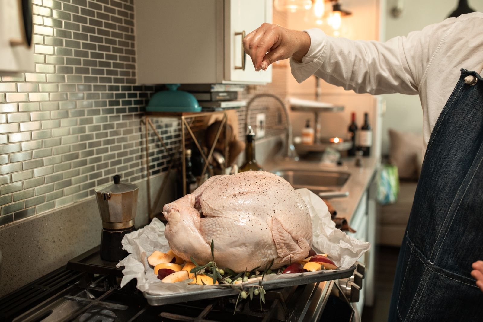 Cook seasoning an uncooked whole turkey on a tray in a home kitchen