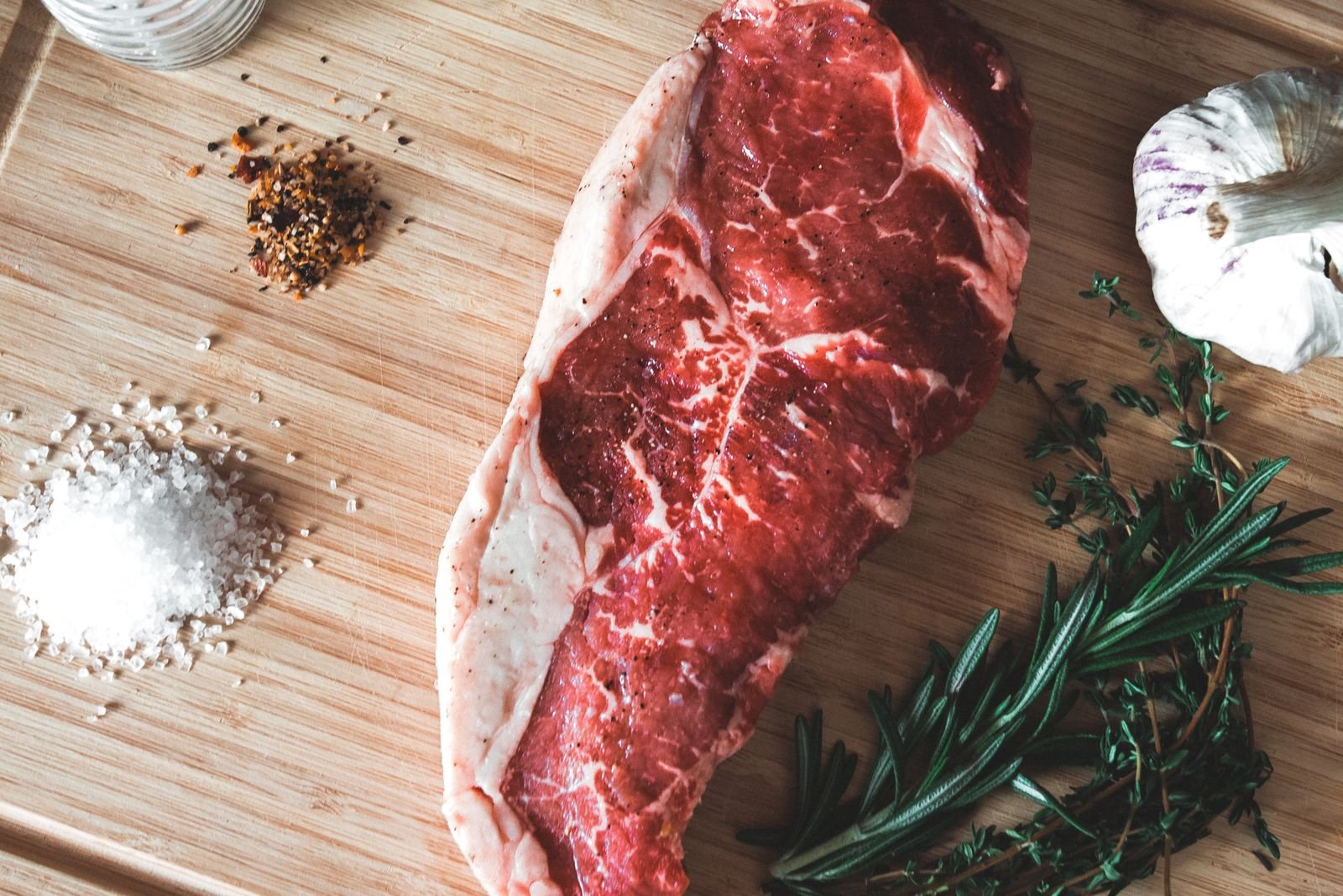 Raw beef steak on a wooden board with garlic, rosemary and spices