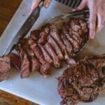 Hands slicing a grilled steak into thin strips across the grain on a chopping board, seen from above