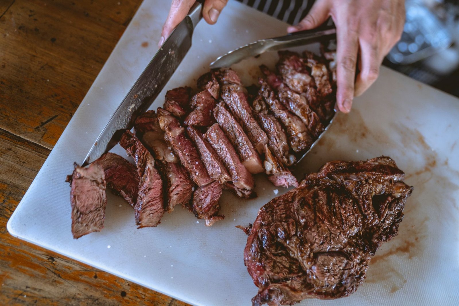 Hands slicing a grilled steak into thin strips across the grain on a chopping board, seen from above