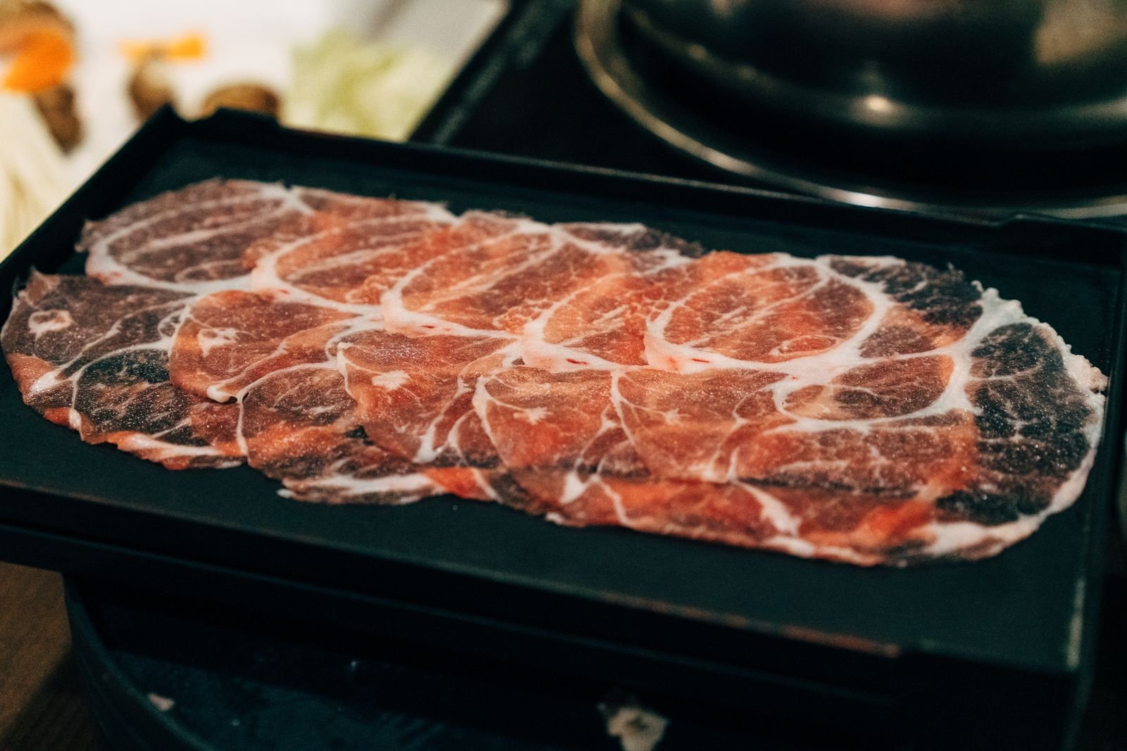 Thinly shaved raw beef slices laid out on a black tray