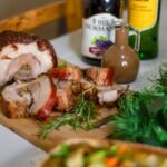 Sliced rolled porchetta roast on a board with rosemary and crisp skin