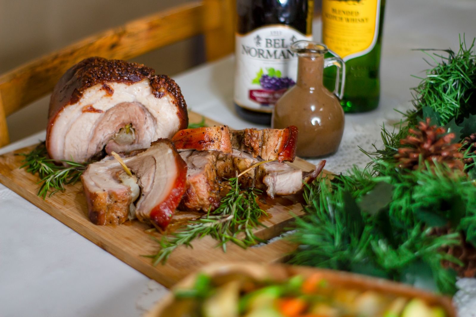 Sliced rolled porchetta roast on a board with rosemary and crisp skin