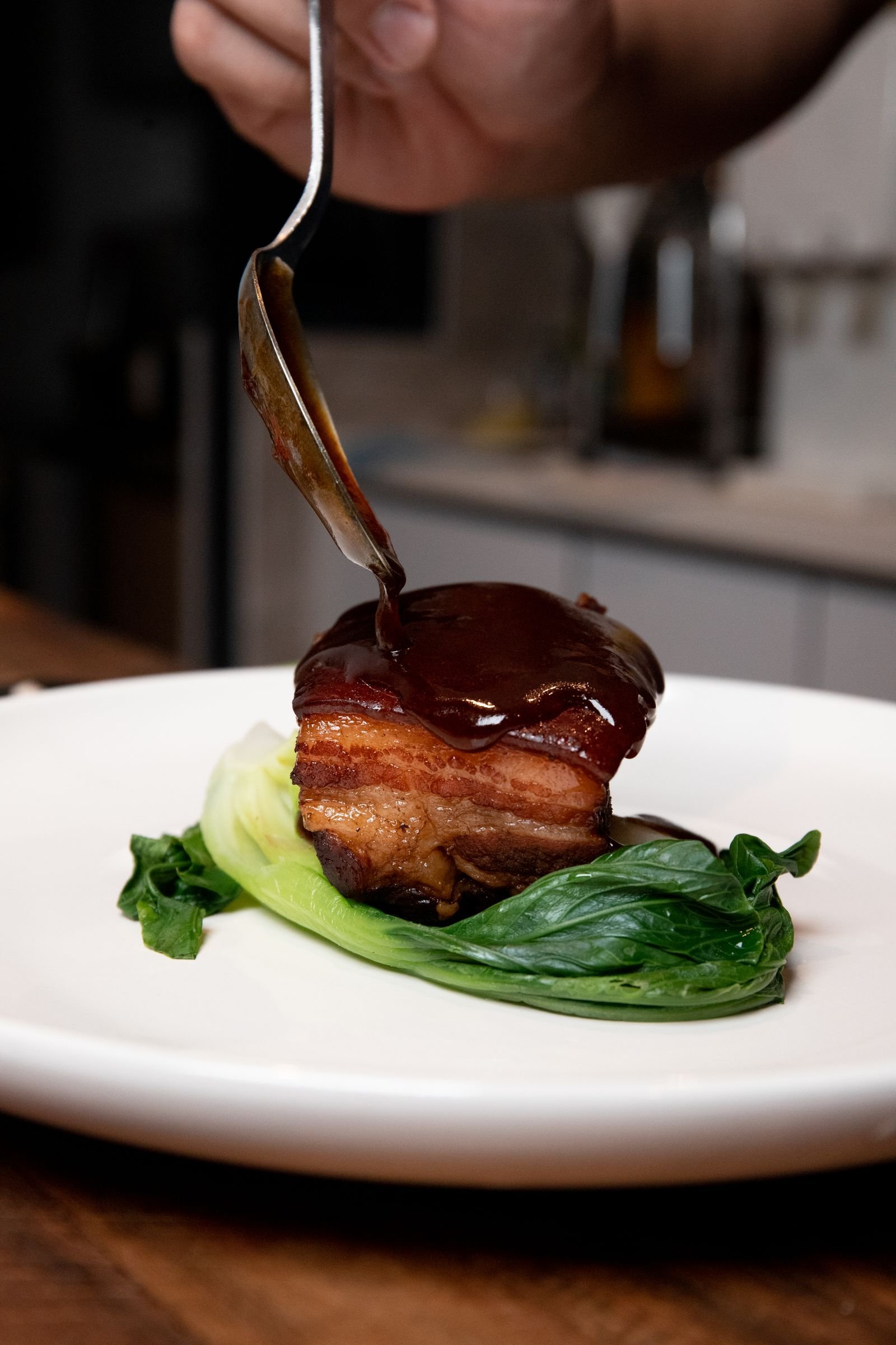 Glazed pork belly in a dark sticky sauce with greens