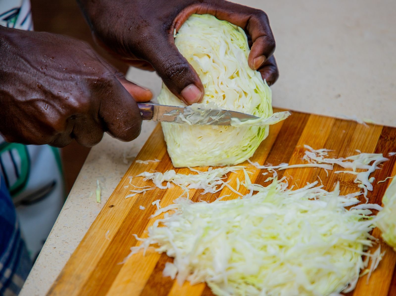 Hands slicing green cabbage into thin shreds on a wooden board
