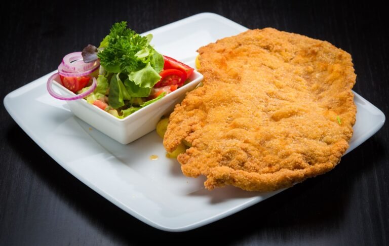 Golden crumbed schnitzel on a white plate beside a small bowl of fresh salad