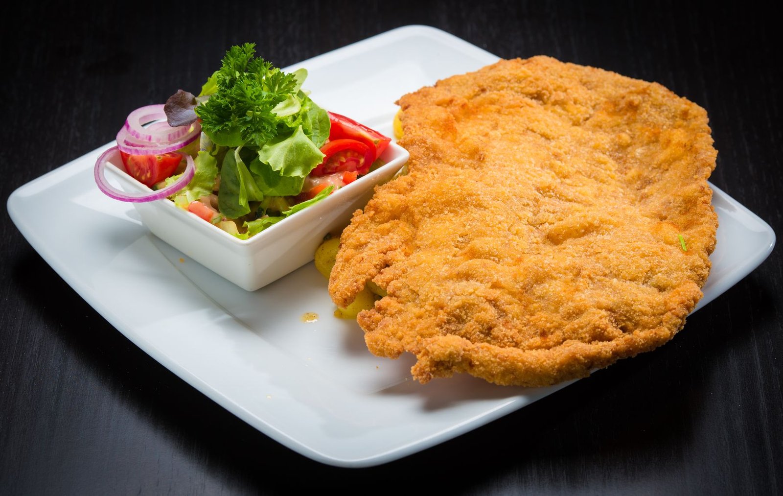 Golden crumbed schnitzel on a white plate beside a small bowl of fresh salad