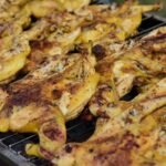 Two spatchcocked chickens lying flat and browning on a barbecue grill