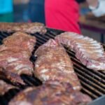 Seasoned racks of pork ribs cooking over the grate with smoke rising