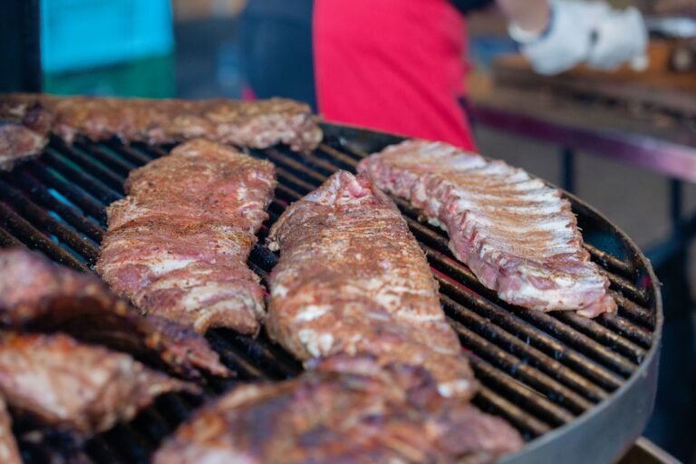 Seasoned racks of pork ribs cooking over the grate with smoke rising