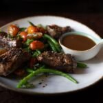 Sliced seared steak with green vegetables and a small jug of pepper cream sauce on a white plate