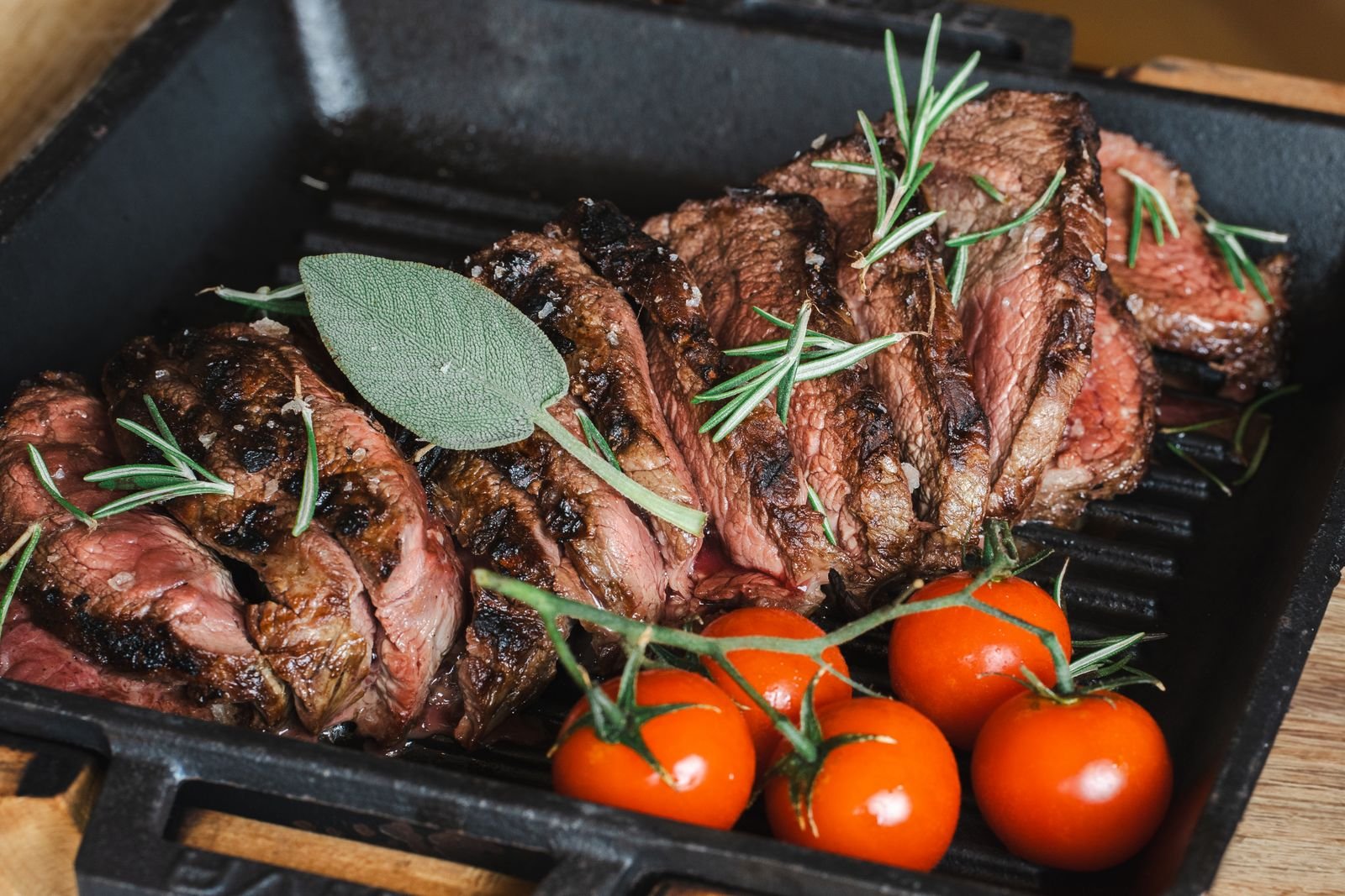 Seared and sliced beef with rosemary sprigs and cherry tomatoes in a dark pan
