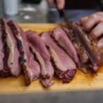 Hand slicing a pink, medium rare beef roast into thin slices on a wooden board